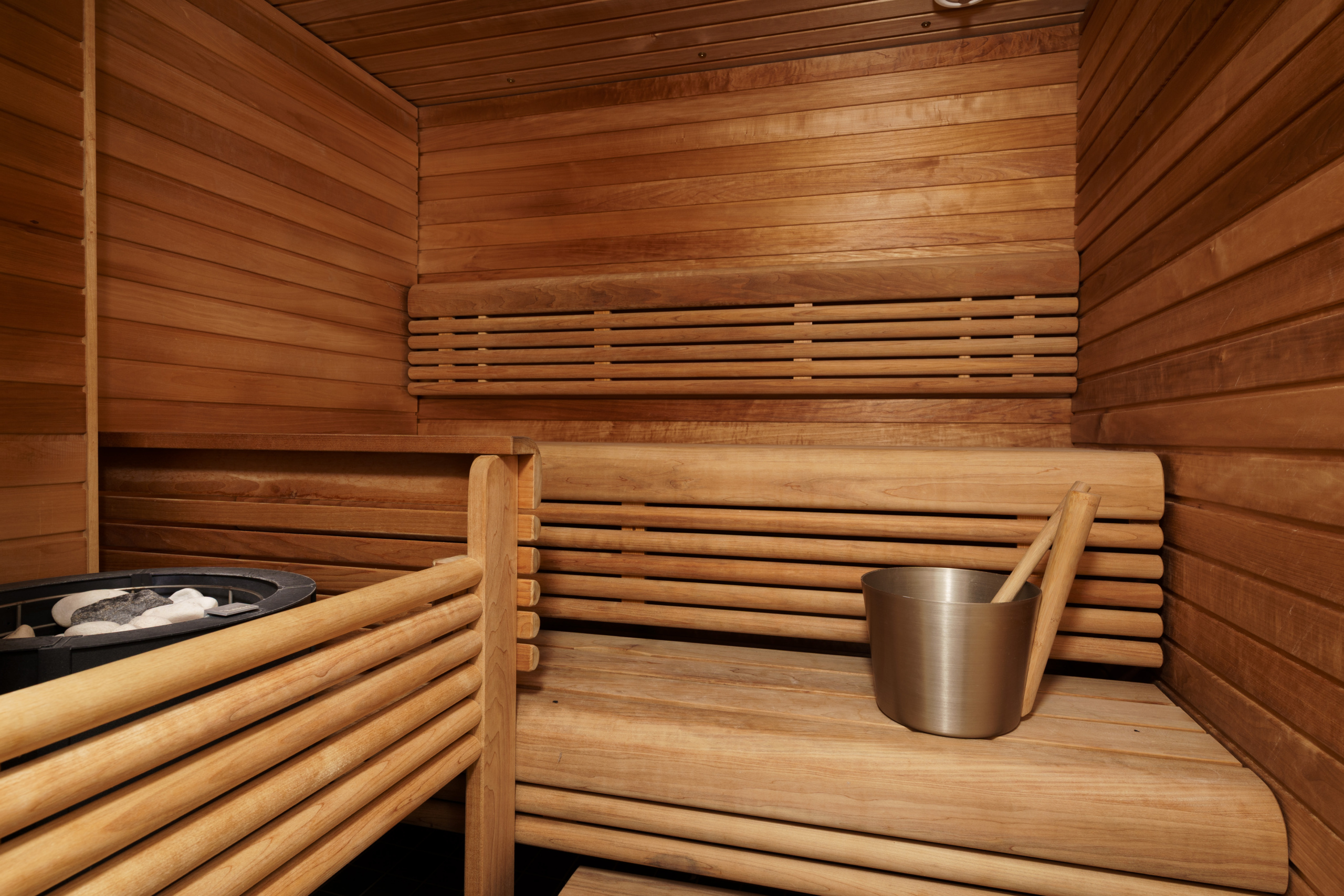 Puupaneloitu sauna, jossa on lauteet, kiuaskivet ja metallinen saunakiulu